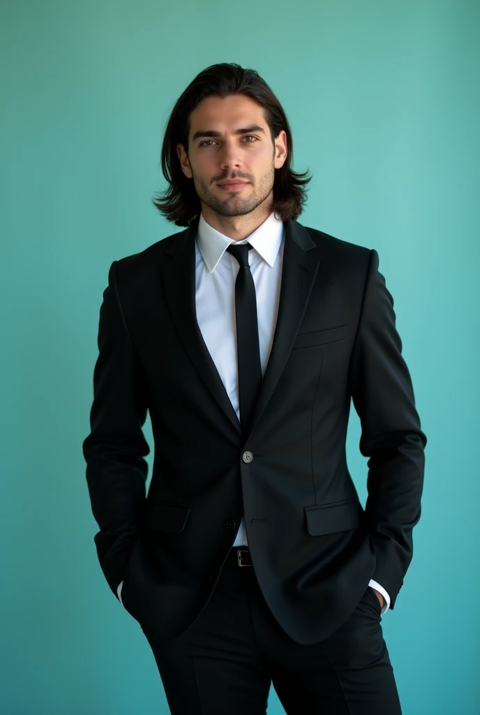 A young man with dark long hair and the bread meduim. He is dressed in a black blazer and tai over a white shirt. The man is positioned against aqua colour backdrop with a subtle and he posing for Facebook profile.