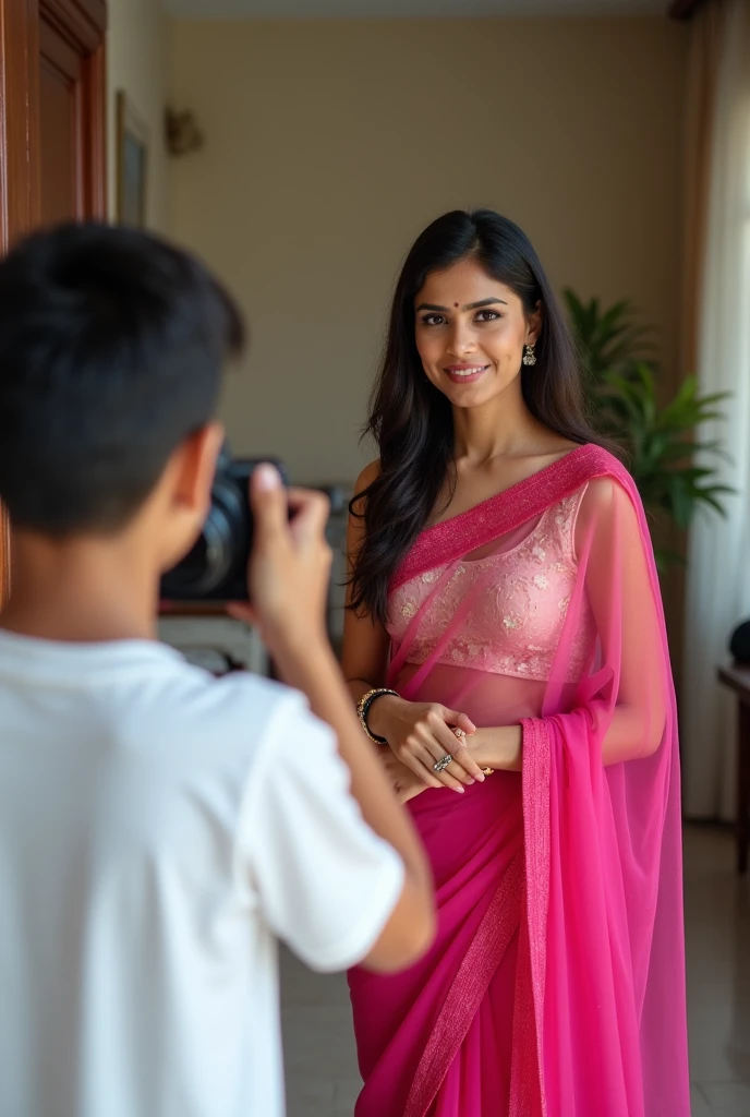 One 3 indian woman wears pink colour transparent saree and blouse, looking at camera and standing infront of a 2 indian boy wears white tshirt who holds  camera in hand, and clicking her photos, in their house at hall.