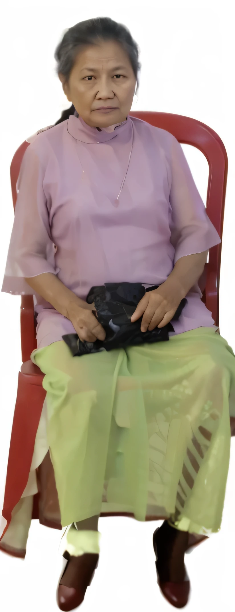 A grandmother from Indonesia with her hair tied back is sitting on a red plastic chair wearing a dress and skirt 