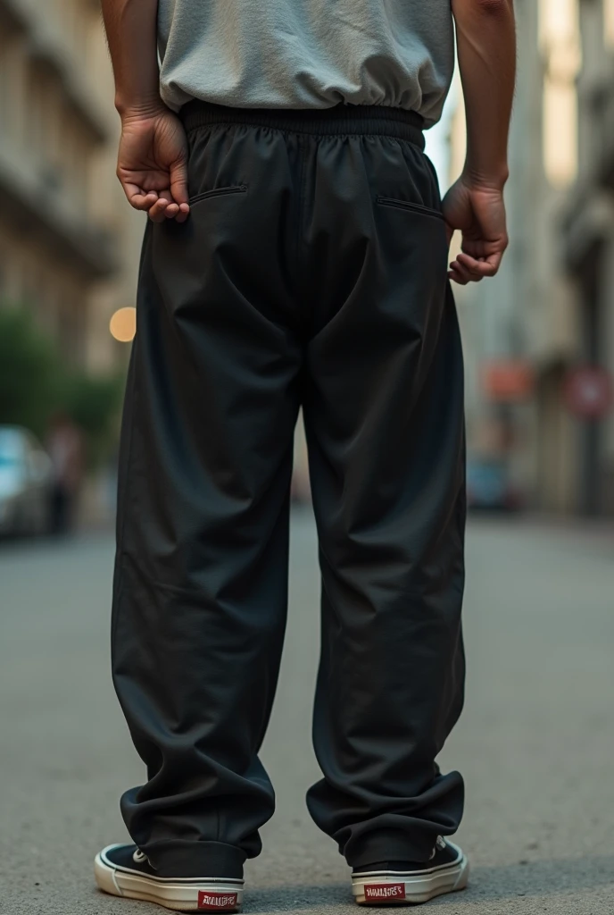 Man from behind wearing skater shoes and loose black pants, putting his hand up his butt under his pants 