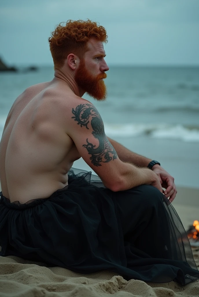 strong bearded redhead man sitting on the sand looking at the sea. he wears gables a black tulle skirt photo with the bonfire lighting appearing.