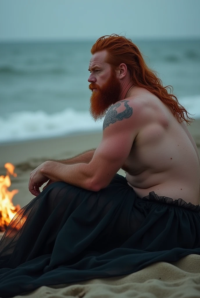 strong fat red-haired bearded man sitting on the sand looking at the sea. he wears gables a black tulle skirt photo with the bonfire lighting appearing. illuminating the body he