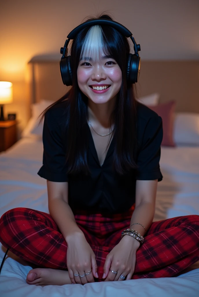 a 2 man with straight black hair and a white streak in the front, with a white smile, sitting cross-legged on the bed, wearing a black blouse with red plaid pants, playing video games and wearing headphones, wearing two bracelets on her arm and a silver wedding ring 