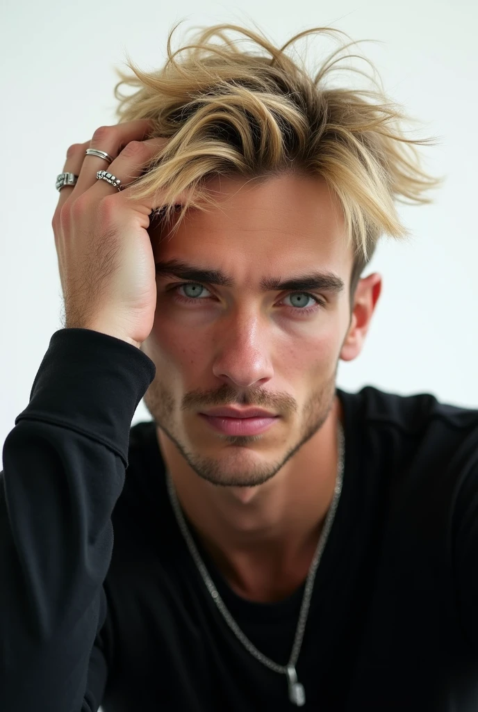 Captured from a low-angle perspective, a close-up of a blond man's face is visible. He is wearing a black long-sleeved T-shirt, a silver necklace, and a silver ring on his right hand. His left hand is updated on his head, adding a touch of warmth to his face. The background is pure white, and the boy's eyes are a piercing blue.