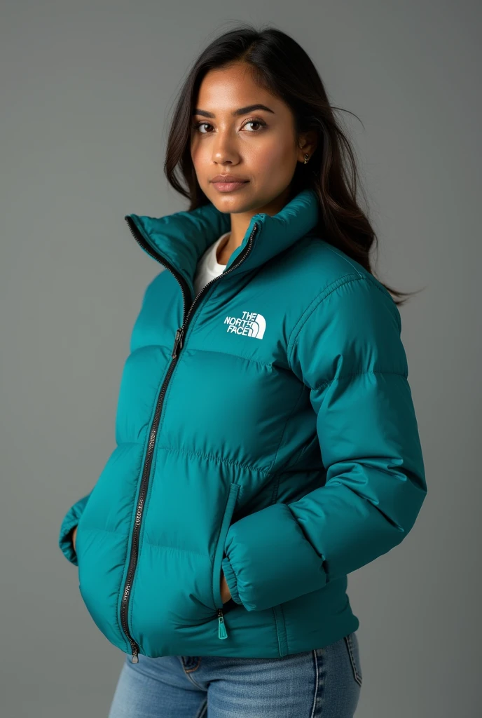 beautiful latin woman, standing straight facing forward,with a closed North Face cold weather jacket in teal, denim jeans pants, on a greyish background. Medium camera shot.