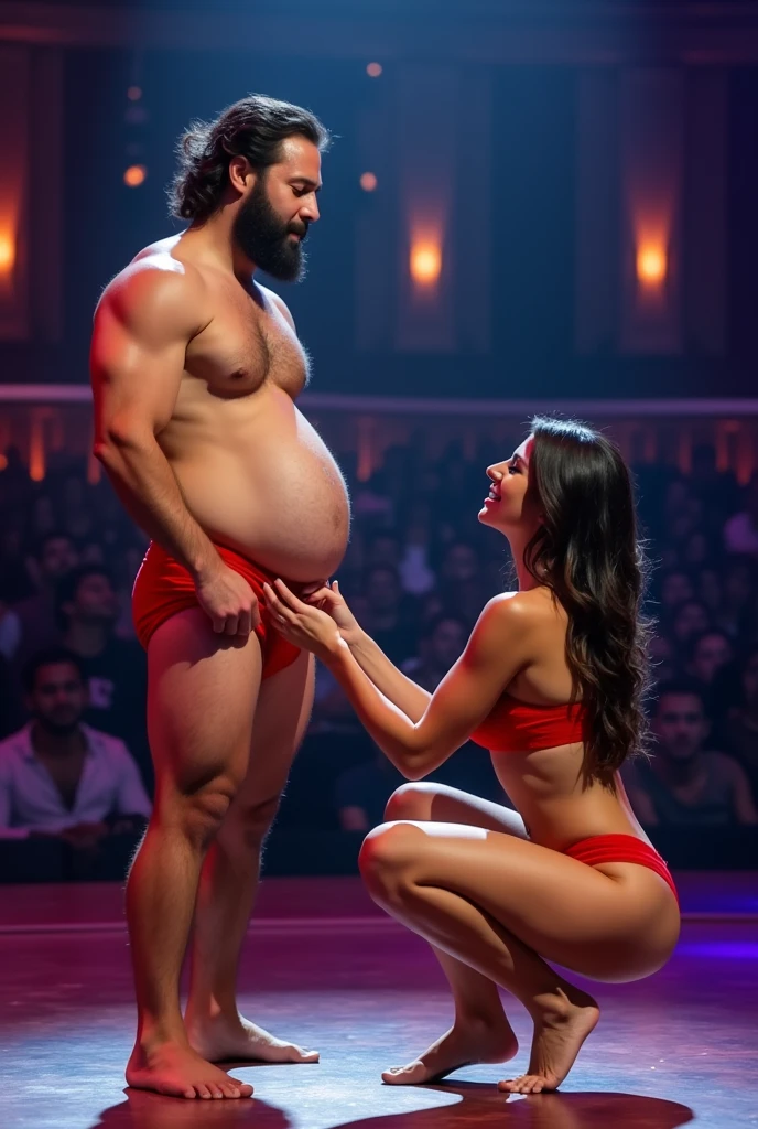 A young Puerto Rican man hairy bearded strong muscular red underwear bulge bulge, having his underwear pulled down naked pubic hair examined by a beautiful woman in red panties crouching in front of him, in performance on a stage of a television program presented by a famous presenter.