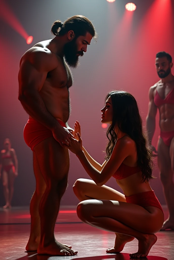 A strong, muscular, bearded, hairy, Brazilian mixed race man in red bulge underwear having his thighs examined by a beautiful woman in red panties crouching in front of him, in performance on a stage of a television program presented by a famous presenter.