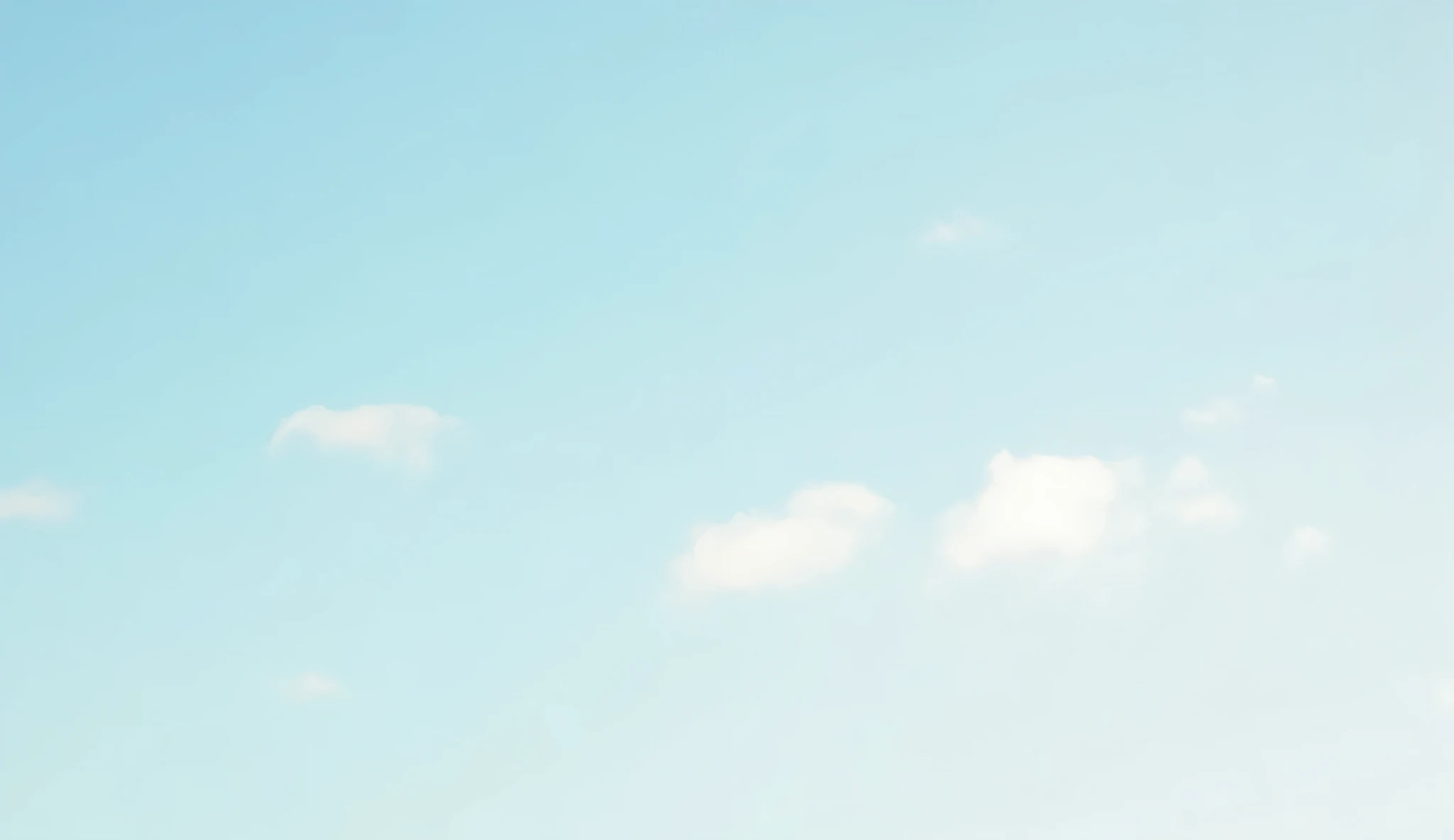 A serene sky with very faint, wispy clouds drifting across a pale blue background. The sunlight is soft, casting a gentle glow across the scene, with the clouds barely noticeable against the vast expanse of the sky.
