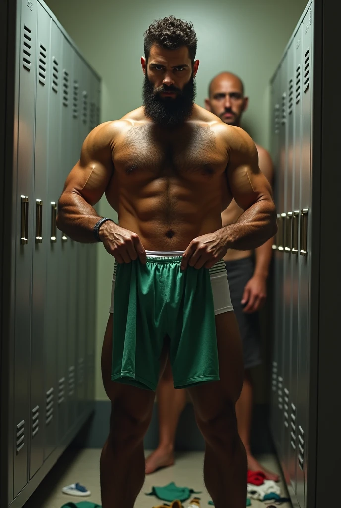 A handsome, muscular, hairy, bearded, mixed-race Brazilian man in white underwear with a pair of long green sweatpants in his hand in front of an open closet, in a small locker room, being discreetly watched in the background by a fat bald man standing very close to us shirtless wearing long jeans. Surrounded by gray cabinets. Clothes lying on the floor.