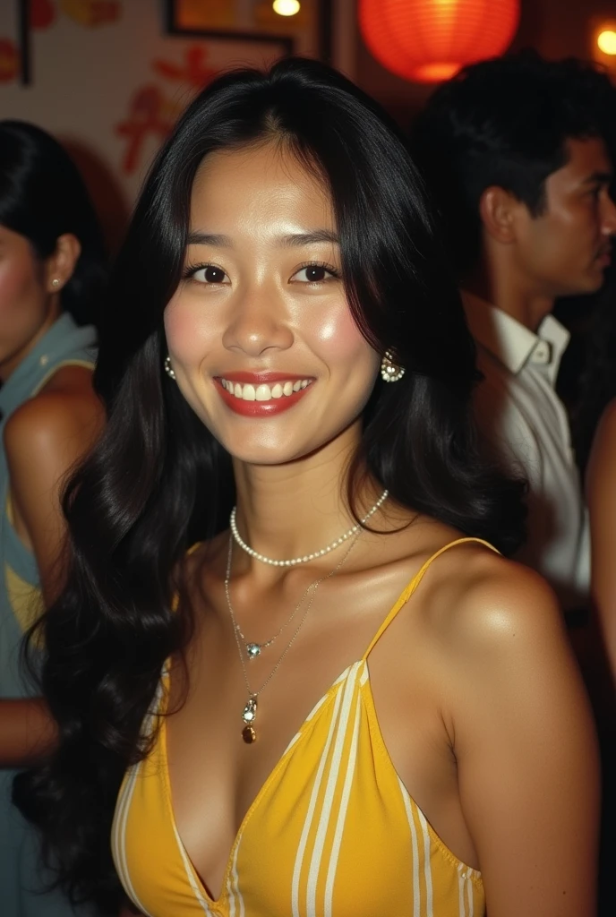 The image shows a vintage photograph, likely from the 1970s or early 1980s, of a young Asian woman at a social gathering. She has a bright smile, long dark hair styled in the fashion of that era, and is wearing a yellow striped halter-style top or dress. The woman's jewelry includes a delicate necklace and what appears to be a longer pearl necklace.
The background is blurry but suggests a crowded, dimly lit environment like a bar or club. There are hints of other people and lights visible behi