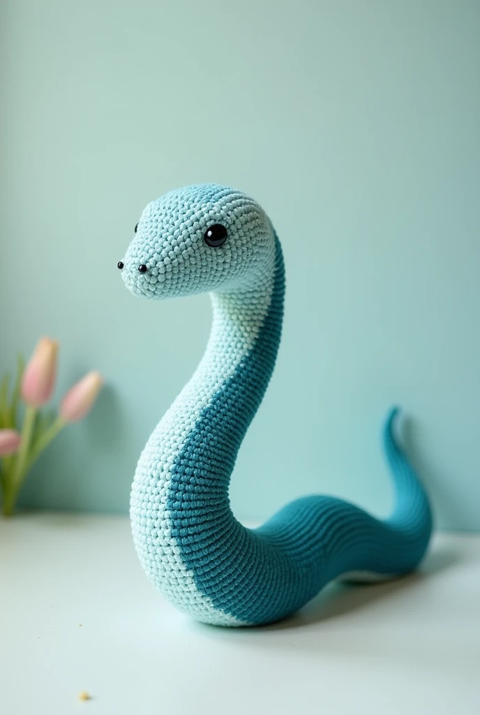 A crochet snake with a light blue head that transitions smoothly into a dark teal at the tip