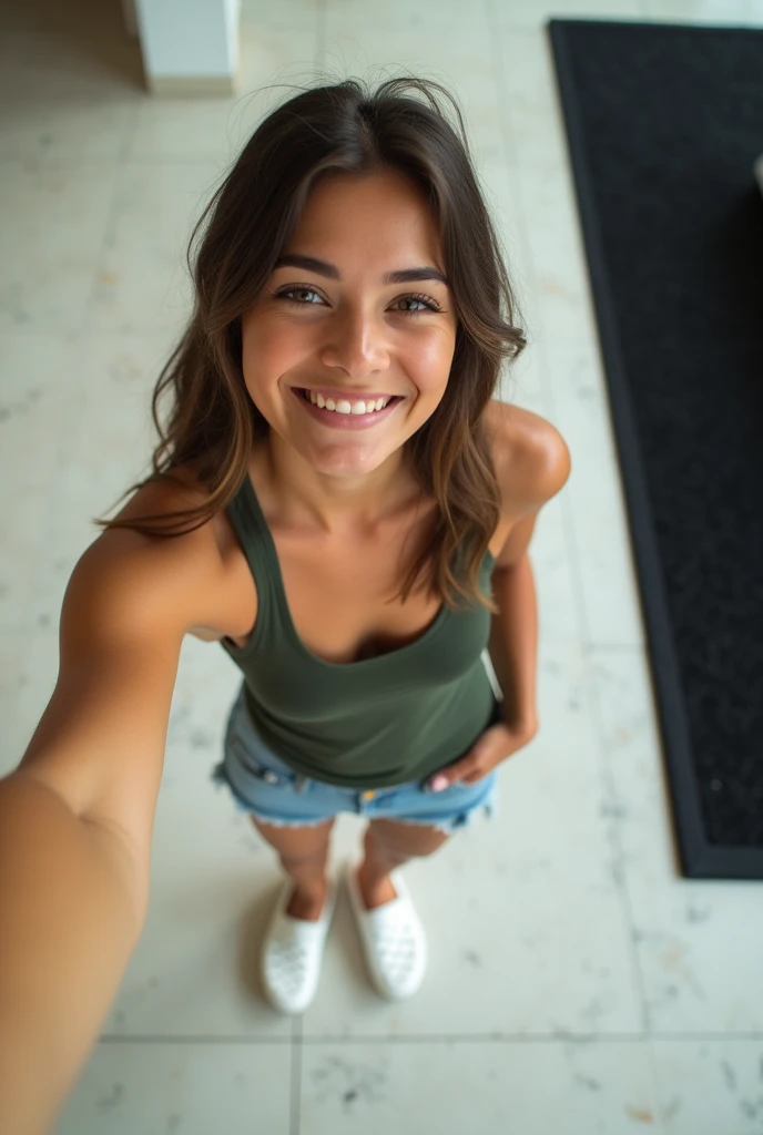 A top down selfie of a girl wearing a dark green tank top and denim shorts, avec des chaussures blanches de style Crocs. Le sol est en marbre ou en carrelage clair, and there is a black carpet on the right side. La personne est debout, leaning slightly forward, with one hand near the waistband of the shorts.