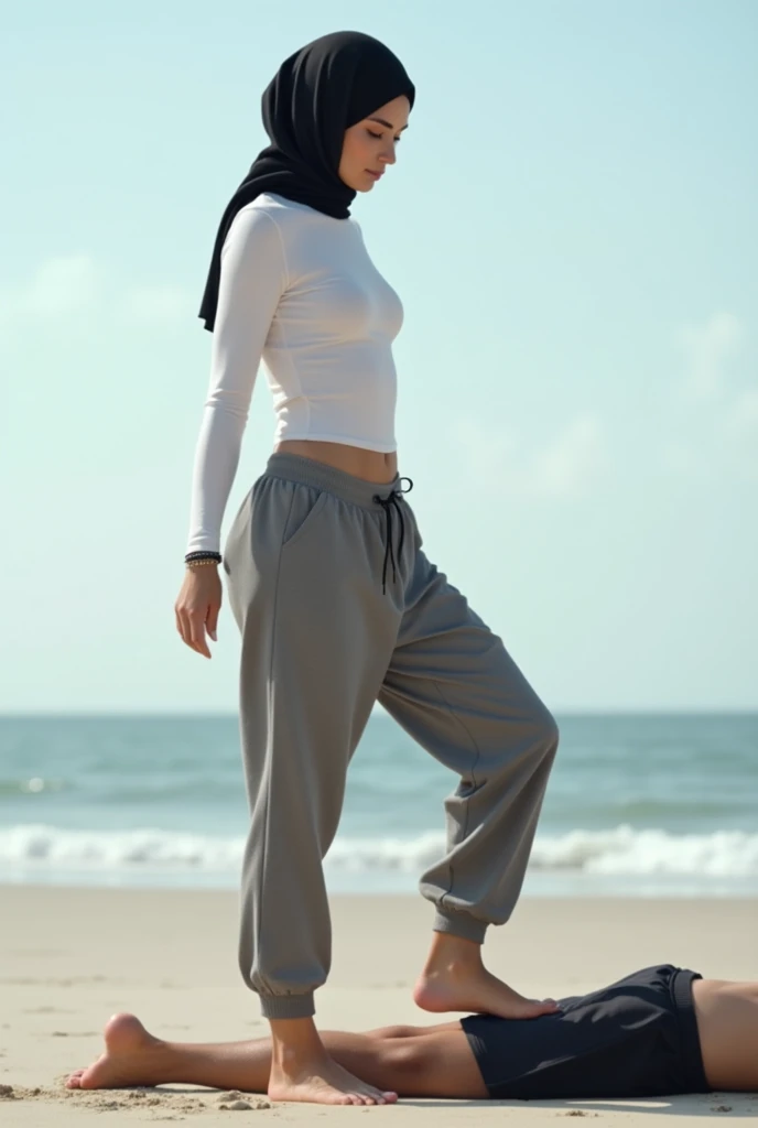 Black headscarf on the beach, grey baggy sweatpants, white long sleeve t shirt, barefoot, sexy and skinny woman. Man lying on his stomach in front of woman. Woman puts her foot on the front of man&#39;s sweatpants. 