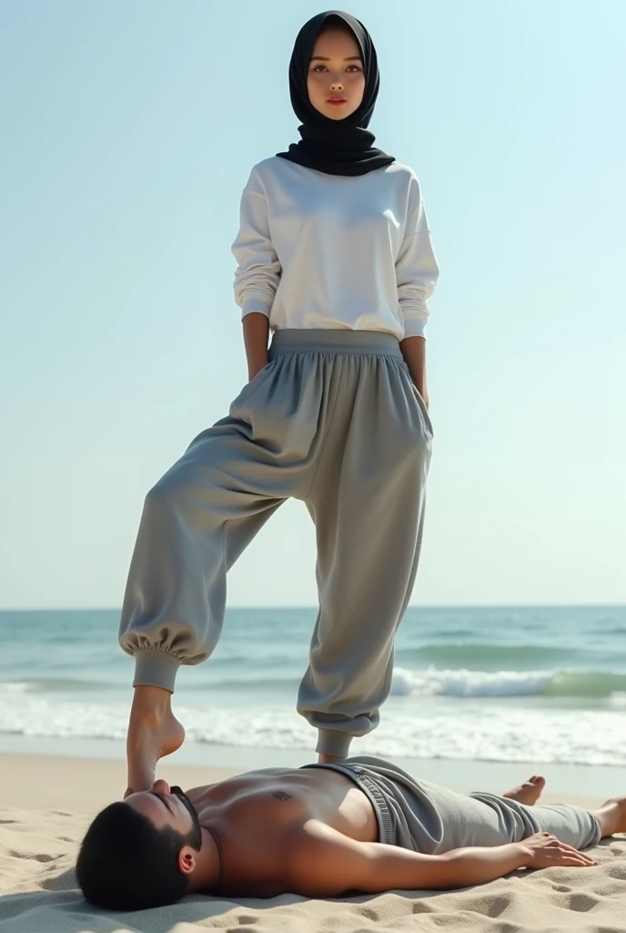 Black headscarf on the beach, grey baggy sweatpants, white long sleeve t shirt, barefoot, sexy and skinny woman. Man lying on his stomach in front of woman. Woman puts her foot on the front of man&#39;s sweatpants. 