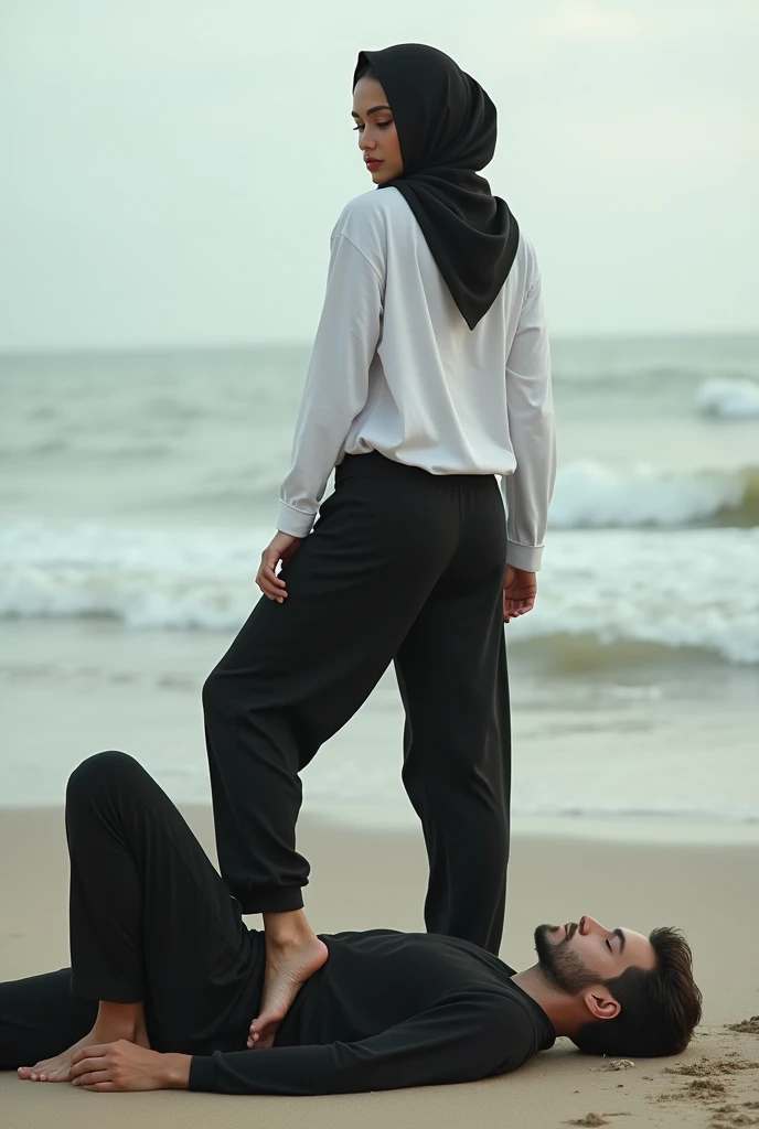 Black headscarf on the beach, black baggy sweatpants, white long sleeve t shirt, barefoot, sexy and skinny woman. Man lying on his stomach in front of woman. Woman puts her foot on the front of man&#39;s sweatpants. 