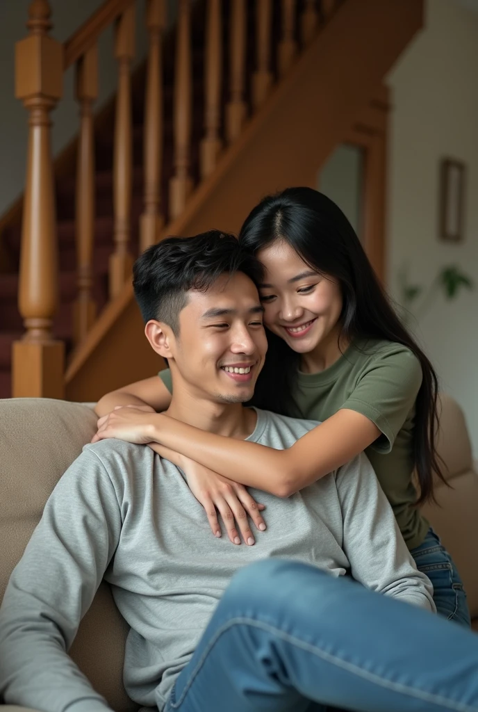 Candid, indoor photograph featuring a young couple in a cozy home setting. The man, with short dark hair is seated on a beige couch, wearing a light gray long-sleeve shirt. The woman, with long straight black hair, is leaning over his shoulders, embracing him from behind, and smiling warmly. She is dressed in a casual green t-shirt and jeans. The background includes a staircase with wooden railings and a partially visible room, adding to the homely atmosphere. The lighting is soft, creating a warm and inviting ambiance.