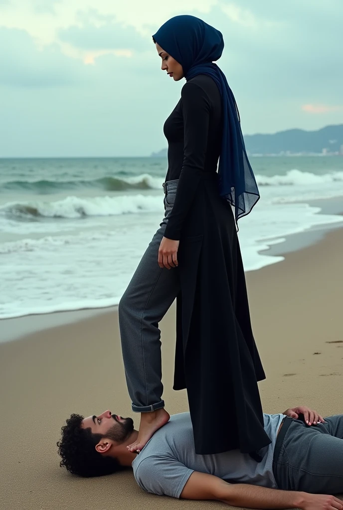 Navy blue headscarf on the beach, black long closed coat, barefoot, Sexy skinny woman. Man lying in front of woman. Woman puts her foot on the front of man's sweatpants.
