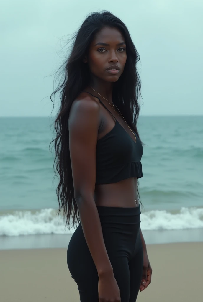 A woman with dark skin, black hair, and a sharp face stands on the beach.