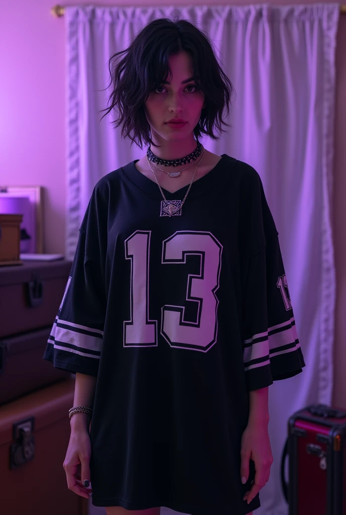 The image shows a person standing in what appears to be a room with a purple-tinted lighting effect. The person has dark, slightly messy, layered hair and is wearing a loose-fitting black sports jersey with white numbers and designs on the front. The number "13" is prominently visible on the jersey. The person also has a choker necklace and appears to have a confident or neutral expression.
In the background, there are some visible items, including stacked suitcases and a white fabric hanging on the wall, possibly serving as a curtain or backdrop. The room has a cozy but slightly cluttered atmosphere. The overall vibe of the image is casual and slightly edgy, with a strong sense of personal style.