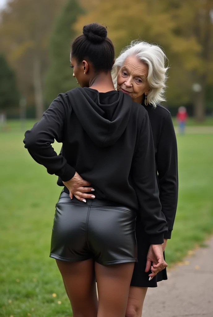 black woman hair in a bun black hoodie black leather short shorts bending over getting fucked in the ass by a old ugly woman in a dress in a park
