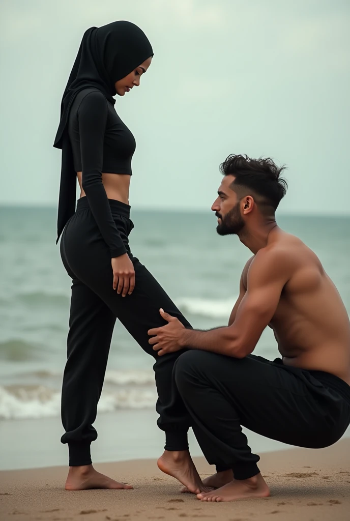 Black headscarf on the beach,black sweatpants, barefoot sexy skinny woman. Man sitting in front of woman. Woman puts her foot on the front of man&#39;s sweatpants. 