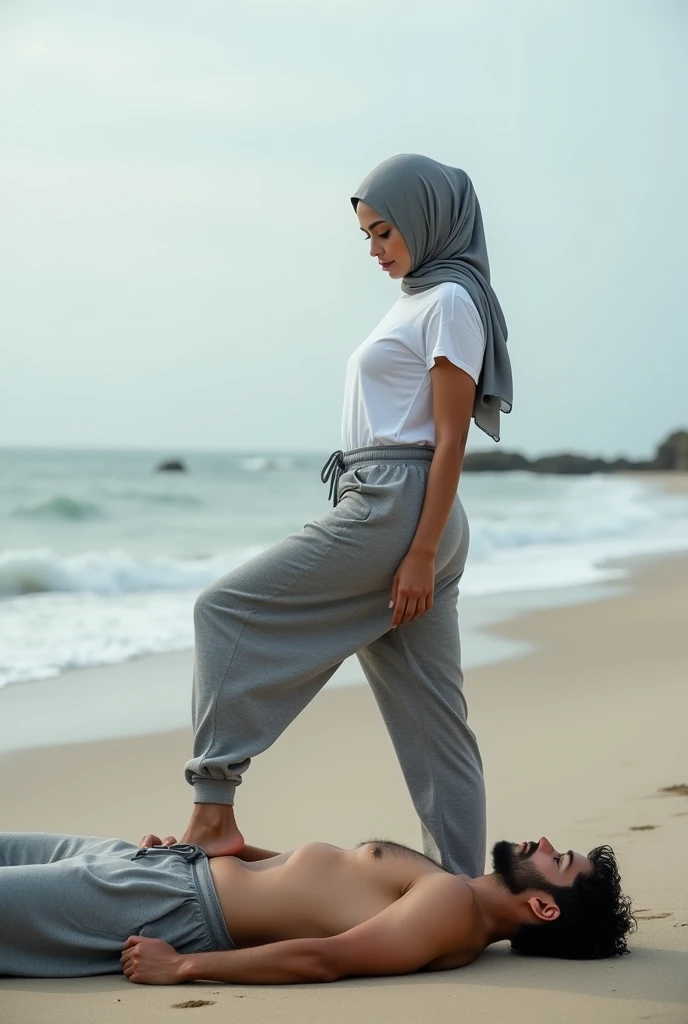 Grey headscarf on the beach, grey baggy sweatpants, barefoot, sexy skinny woman in white long sleeve t-shirt. Man lying in front of woman. Woman puts her foot on man's sweatpants.