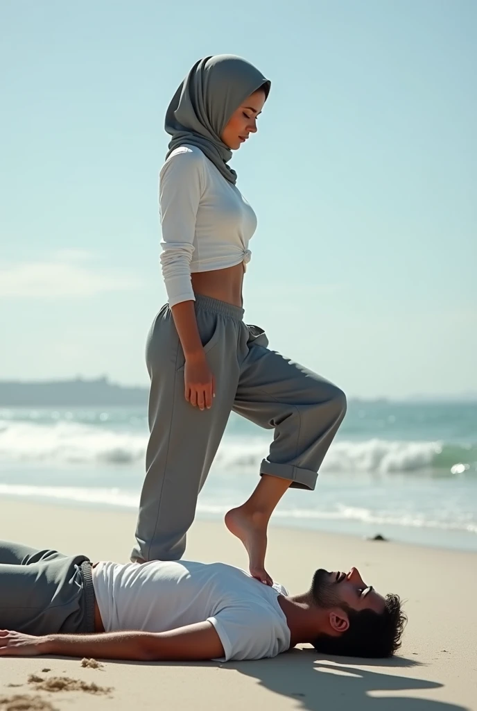 Grey headscarf on the beach, grey baggy sweatpants, barefoot, sexy skinny woman in white long sleeve t-shirt. Man lying in front of woman. Woman puts her foot on man's sweatpants.