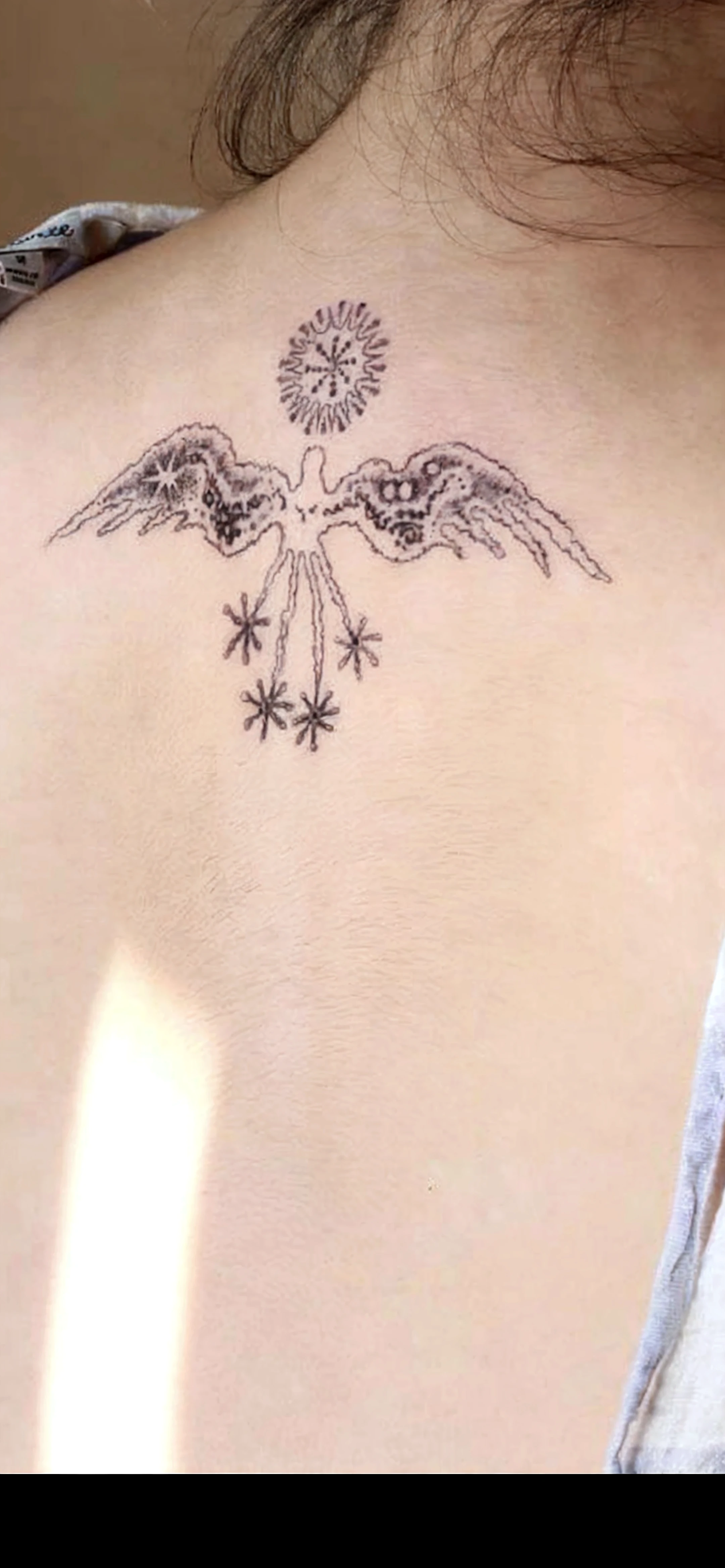 downtown: In the center of the tattoo, a pair of large angel wings is drawn. The left wing is fully open, while the right wing is folded, as if protecting something. The wings follow the contour of the decal of a pair of hands. Outer Circle: Around the wings, there is a circle that imitates the tips of a compass rose, with four main directions. dates: At each of the four points of the circle, the following dates are written in Roman numerals (21/2/2024: xxi.II.MMxxiV, 07/07/1963: VII.VII.MCMLXIII, 12/10/1963: XII.X.MCMLXIII, 30/10/1983: xxx.X.MCMLXxxiII)
