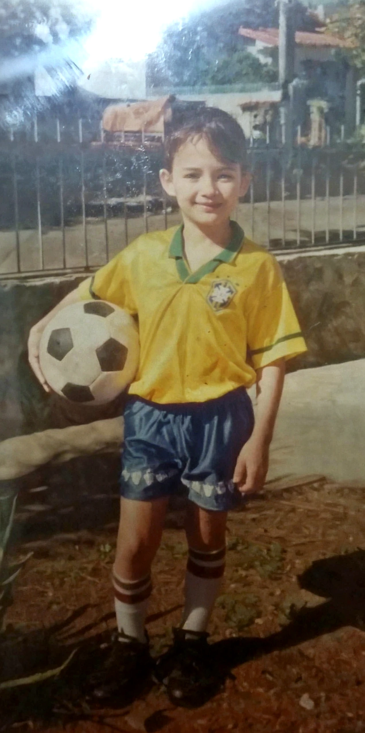 Write S.B on the big sinebord in the bush with the boy holding soccer ball on his t shirt write SONUX at the back of his shirt with some bananas on the side