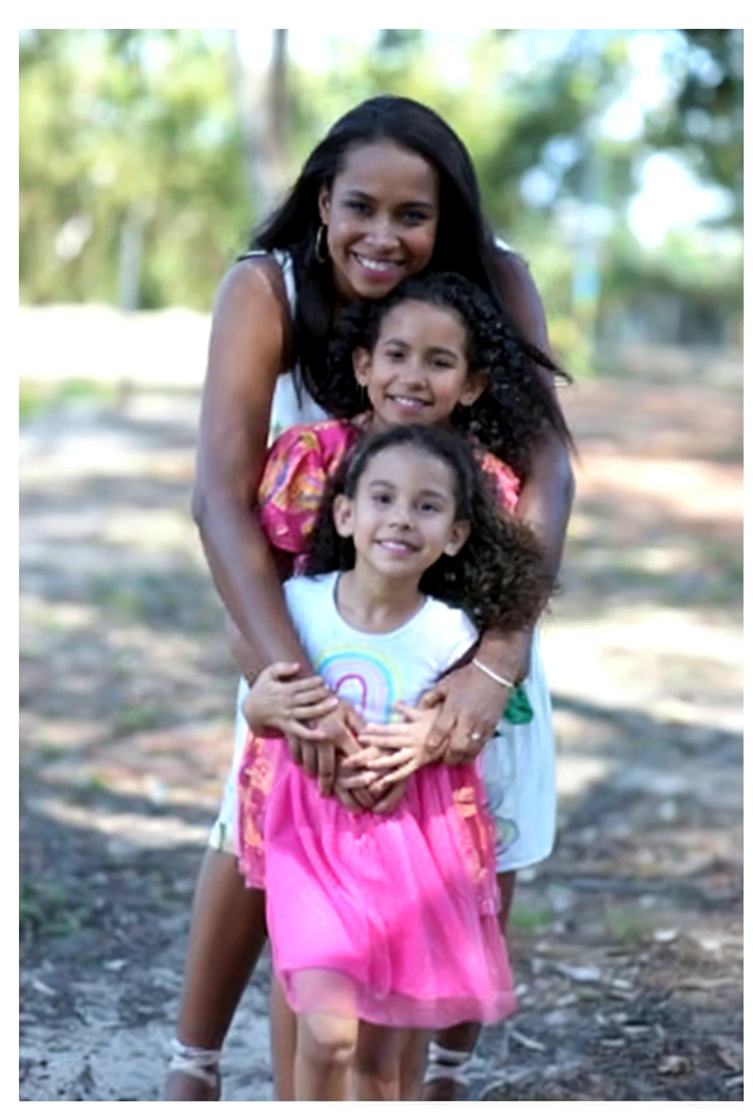 Create a realistic, heartwarming image of a Haitian mother accompanied by her for Mother's Day. The mother should have dark skin, expressive eyes, and natural hair styled in a traditional or modern way. She is wearing a colorful dress with vibrant patterns that reflect Haitian culture. The , around 5 years old, has a joyful expression, matching the mother's appearance with similar skin tone and hair texture. They are sharing a tender moment, such as the mother holding the in a loving embrace or walking hand-in-hand in a picturesque Haitian village. The background includes elements like tropical flora, traditional houses, or a serene beach, highlighting the beauty of Haiti. The overall scene should convey warmth, love, and the special bond between mother and .