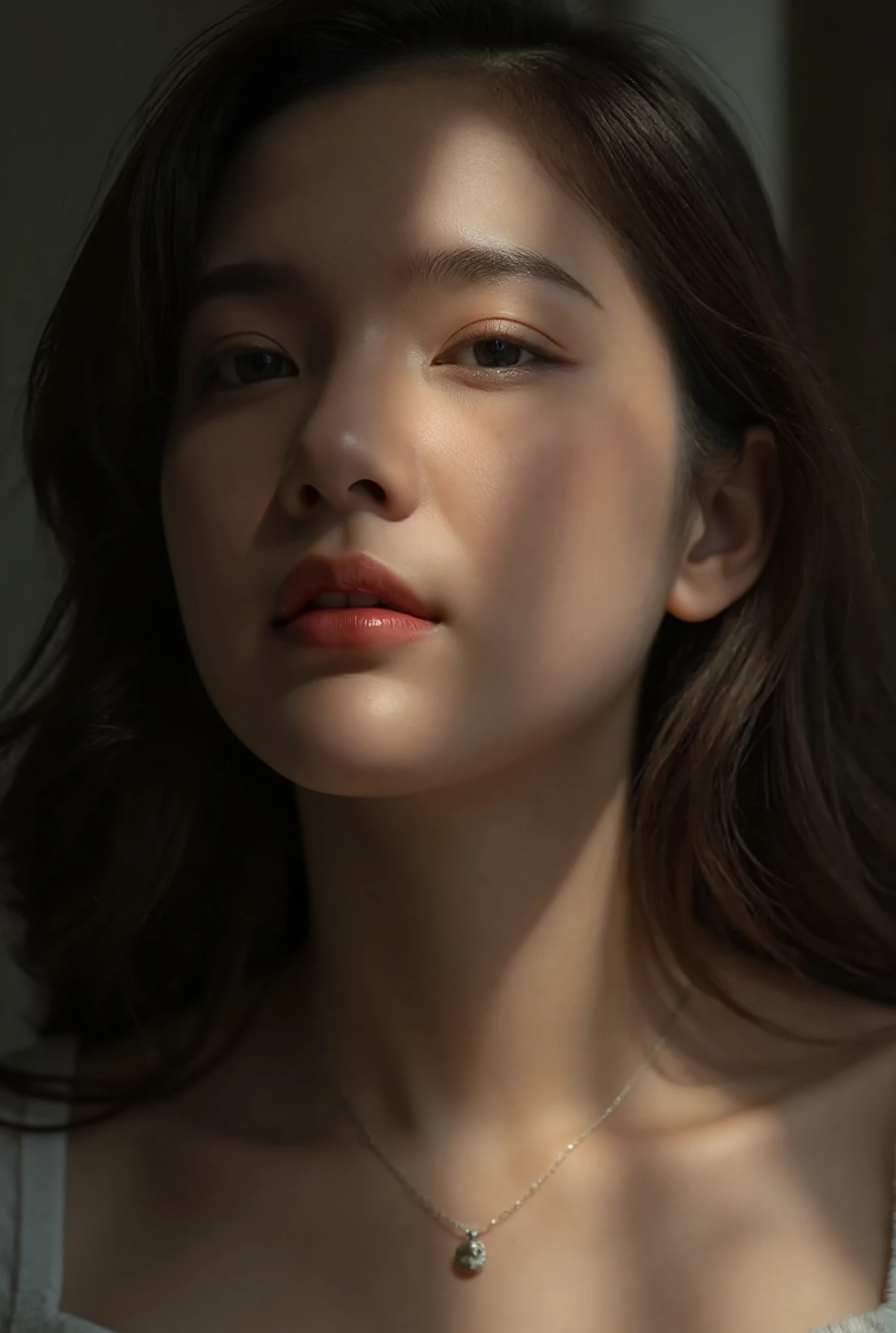 A close-up portrait of a young Thai woman looking upwards with a thoughtful expression. Her face is softly illuminated, with shadows cast across her features, adding depth and a sense of mystery to the image. She has long, slightly wavy hair framing her face, and her eyes are highlighted by natural light. She wears a delicate necklace with a small pendant, complementing her subtle makeup and glossy lips. The overall mood of the photo is contemplative and serene, with a dreamy, artistic quality.