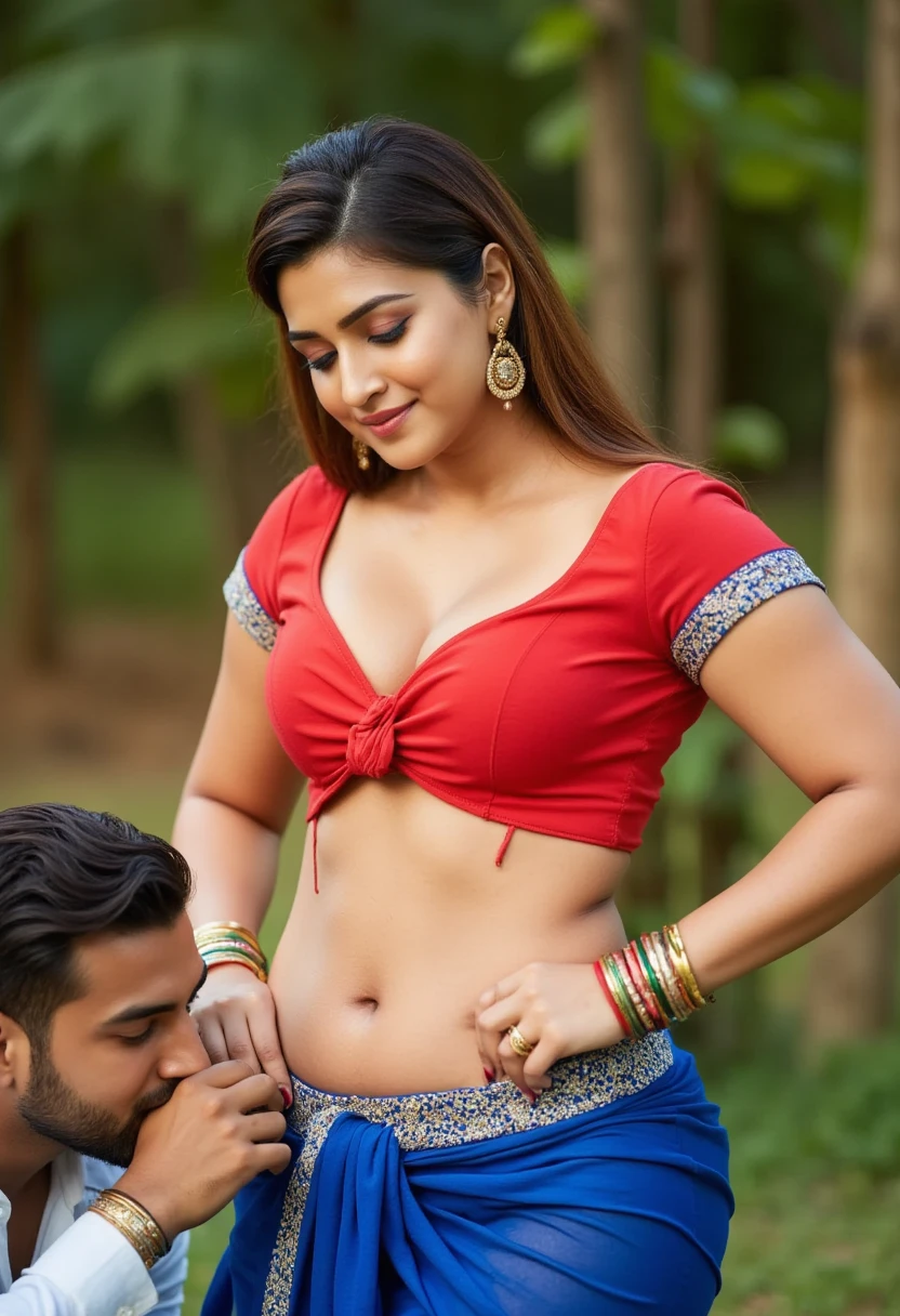 A strong Indian girl with long hair styled in an elegant updo, looking softly downward with a warm expression. She is wearing a traditional red blouse with short sleeves and a knotted front, paired with a matching blue draped bottom piece featuring an embellished waistband. Her midriff and navel are visible, highlighting her toned waist and curvy figure. She wears traditional Indian jewelry, including gold dangling earrings and a set of colorful bangles. Detailed, smooth skin with a natural glow, expressive and perfectly shaped eyes, and a small bindi on her forehead. Next to her, a man is bending down slightly, placing a gentle kiss on her navel, his hand resting on her hip in a gesture of closeness and affection. The setting is outdoors with natural greenery in soft, diffused lighting