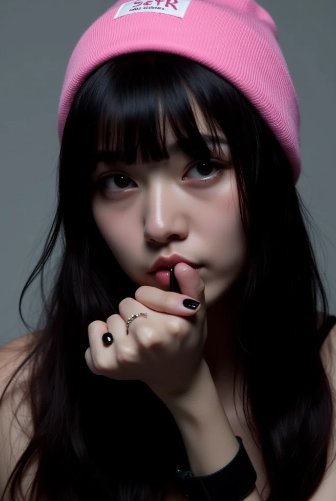 a close-up portrait of a young woman with long dark hair and bangs. She is wearing a pink beanie with a white logo on it. Her face is turned slightly to the side and she is looking directly at the camera with a serious expression. Her nails are painted black and she has a ring on her finger. The background is a plain grey color. The overall mood of the image is dark and edgy. aesthetic posing