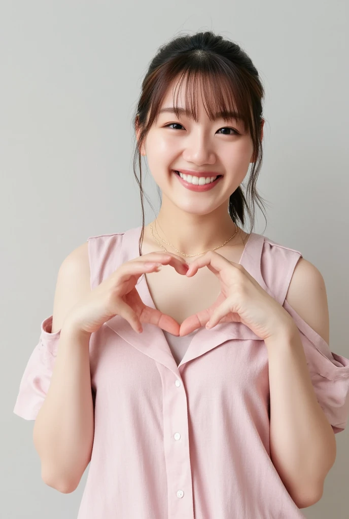 A smiling woman poses alone wearing off-the-shoulder pajamas in pastel colors that convey warmth simply by touching them softly and softly, making a firm, large heart shape with both hands, and holding them in front of her chest, View above collarbone、The background is a monotone 、
