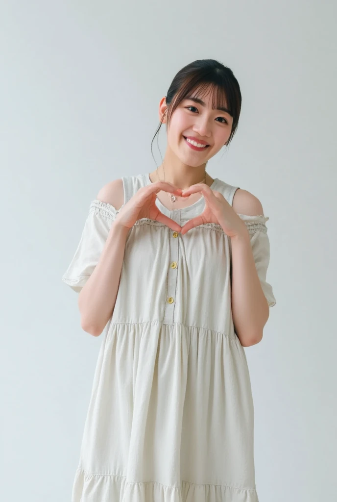 A smiling woman poses alone wearing off-the-shoulder pajamas in pastel colors that convey warmth simply by touching them softly and softly, making a firm, large heart shape with both hands, and holding them in front of her chest, View above collarbone、The background is a monotone 、
