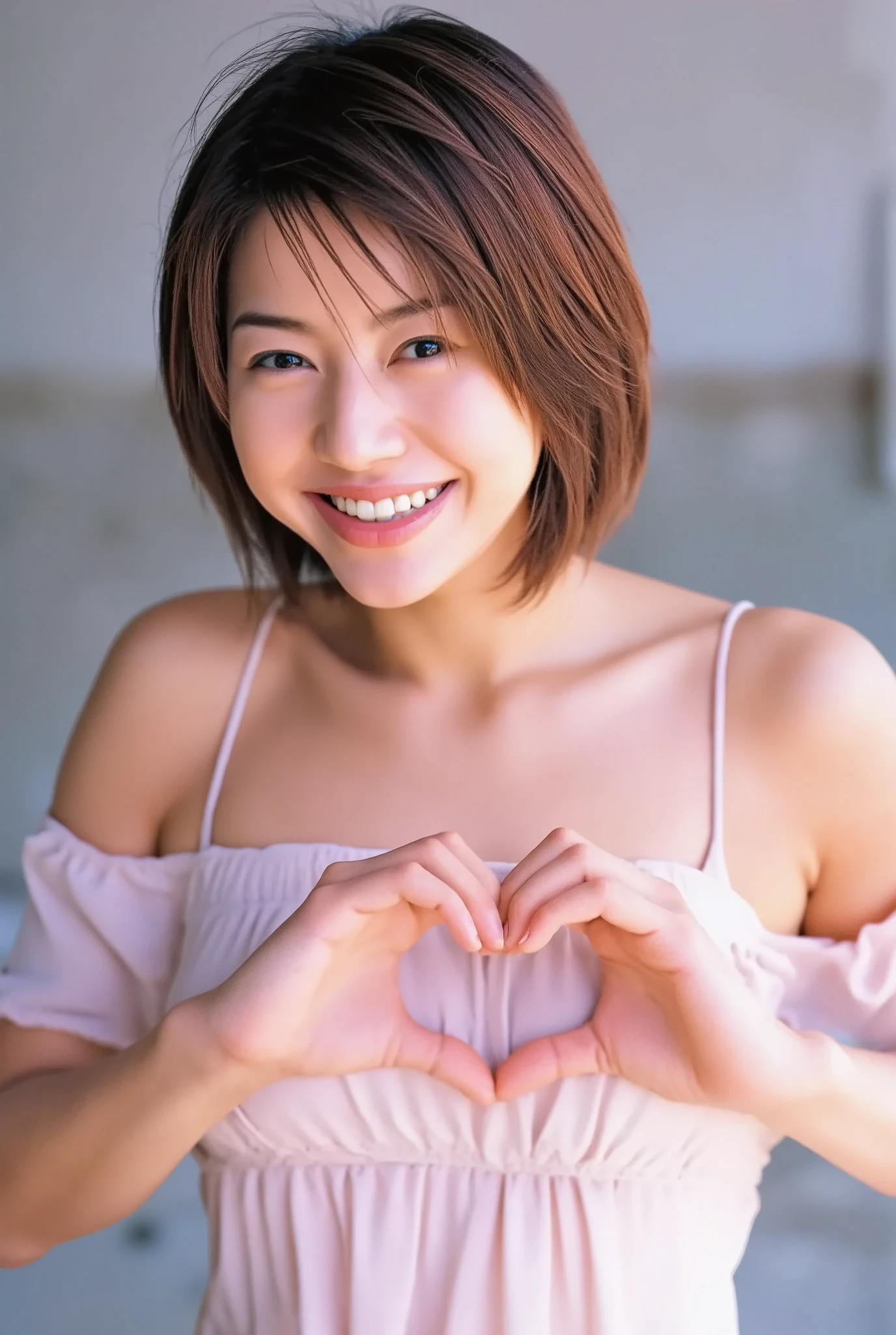 A smiling woman poses alone wearing off-the-shoulder pajamas in pastel colors that convey warmth simply by touching them softly and softly, making a firm, large heart shape with both hands, and holding them in front of her chest, View above collarbone、The background is a monotone 、
