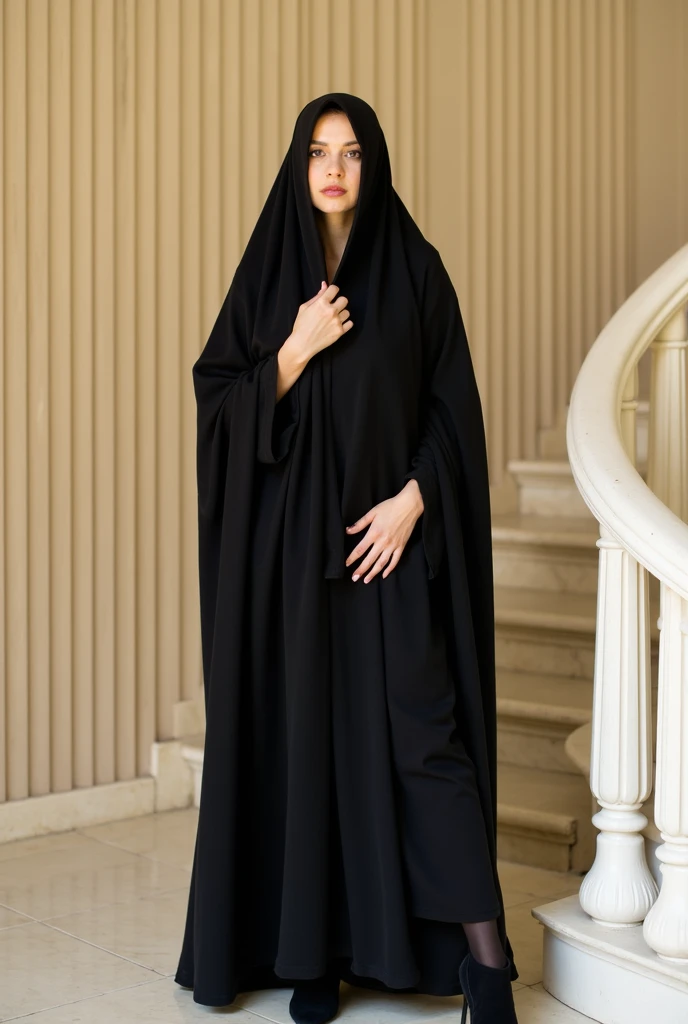 She is wearing a traditional black veil that covers her head and body. The woman is wearing black tights and black high heels. Her hands are positioned so that one is resting on her chest and the other on top of it, her fingers lightly touching the fabric of her veil. She has a neutral expression and is looking directly at the camera. Her eyes are partially visible, with a subtle slant. The light is natural daylight, casting shadows on the right side of her body and creating a high-contrast effect on the fabric of her dress. The background features a beige wall with vertical ridges, and a curved white railing or staircase is visible on the right side of the image. The floor appears to be marble with light-colored tiles. The overall composition is centered, with the subject occupying most of the frame, emphasizing the traditional dress against the plain background.