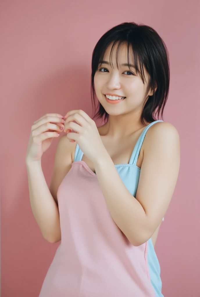 A smiling woman poses alone wearing one-shoulder pajamas in pastel colors that convey warmth simply by touching them softly and softly, making a firm, large heart shape with both hands, and holding them in front of her chest, View above collarbone、The background is a monotone 、
