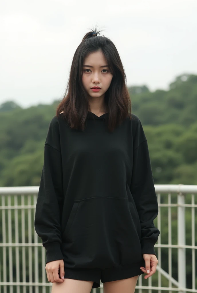 a young woman with long black hair, wearing a underbob cut black hoodie and a pair of shorts. She is standing in front of a white metal fence, with her arms  , adding a pop of color to her face. The backdrop is a lush green forest, with a white sky , hair cover one eye , shy , cute pose , bareface no make up , taunting , 