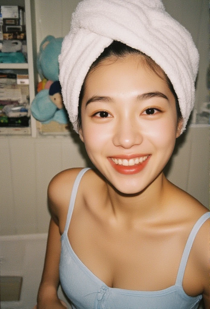 I'm standing in what seems like a bedroom, getting ready for a photo. I've got a towel around my head, probably just out of the shower. My skin is light, and people might guess I'm from Southeast Asia. I'm wearing a light-blue, cropped tank top, feeling relaxed with a hint of cheer in my eyes. One hand's on my hip. The room's got a cozy vibe with a shelf full of stuff and a cute, light-blue plush toy with a cartoon face peeking out. The light's not too bright, more like regular indoor lighting, with some shadows playing around. It all feels pretty casual and personal.