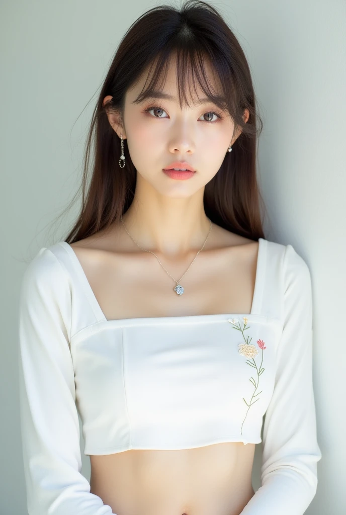 a portrait-style photograph featuring a gorgeous Asian woman with light skin and straight, shoulder-length brown hair with bangs. She is wearing a white, long-sleeved top with a cropped design, revealing a small portion of her midriff. The top has subtle embroidered details on the left side. She accessorizes with a delicate necklace featuring a small pendant and matching earrings. The background is plain and light-colored, which keeps the focus on the subject. Her expression is neutral, and she is looking directly at the camera.