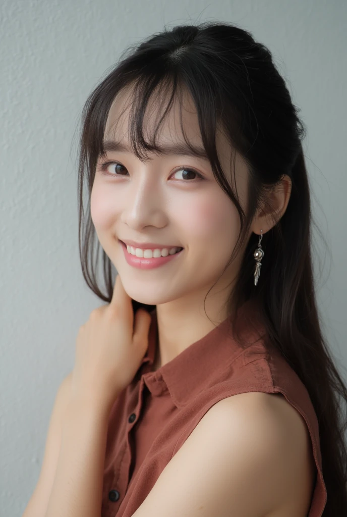 A close up portrait shot of a cute asian dark-haired woman with bangs with long dark brown hair, smiling. She's smiling slightly, her eyes are squinted, adding a touch to her face. Her eyes are wide open and her eyes huddled over her lips. Her lips are painted, a light pink shade, showing her teeth. She is positioned right in an angled way to the left of her face, on her right ear. Her right ear is encased in dangling dangling silver earrings. The woman's upper right elbow is encrossed. She wears a sleeveless brown shirt with a maroon stripe. The shirt is light-red with a collar over it. The wall behind the woman is a light gray color, creating a peaceful white background that accents her features.