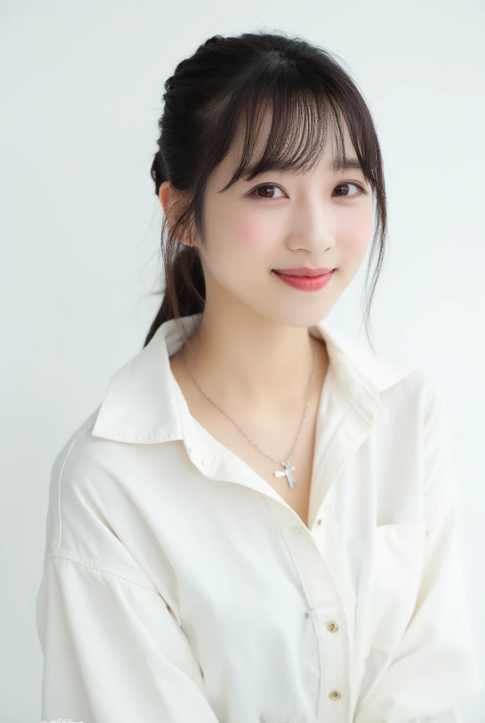 A seated close-up portrait of a cute young Asian woman stands against a stark white backdrop. The woman has dark brown hair with bangs, lighter eyes with darker brown eyebrows, and dark brown eyes. She is smiling, her lips are slightly pursed, and she has a ringed, pink cheeks. The women's hair is pulled back behind her, her bangs are pulled back at the top and cascades over her forehead. She Is wearing a white long-sleeved long-ved shirt that is buttoned up with a collar and buttoning down its chest. She appears to be posing for a camera. Her right arm is turned at the side of the frame, and her left wrist is tucked beneath her waist. She has a silver necklace with a small gray charm. The necklace is on her lower lip area, while one of her ears is open on the right.