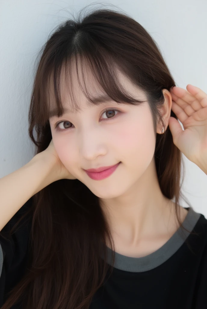 An overhead view of an Asian cute woman, with bangs and long, straight brown hair reaches all around her shoulders. She's head in two rows, her left side by a small amount of water on her face. Her eyebrows, their eyes are slightly turned to the side, with a few of them perched on their right ear. The woman's right arm is positioned in front of her face, her right hand resting on her left ear. She is smiling, her lips slightly lighter purple. She has a soft, smooth texture all she is holding in the air. She wears a black t-shirt with a dark-gray trim. The background behind her is a light white wall.