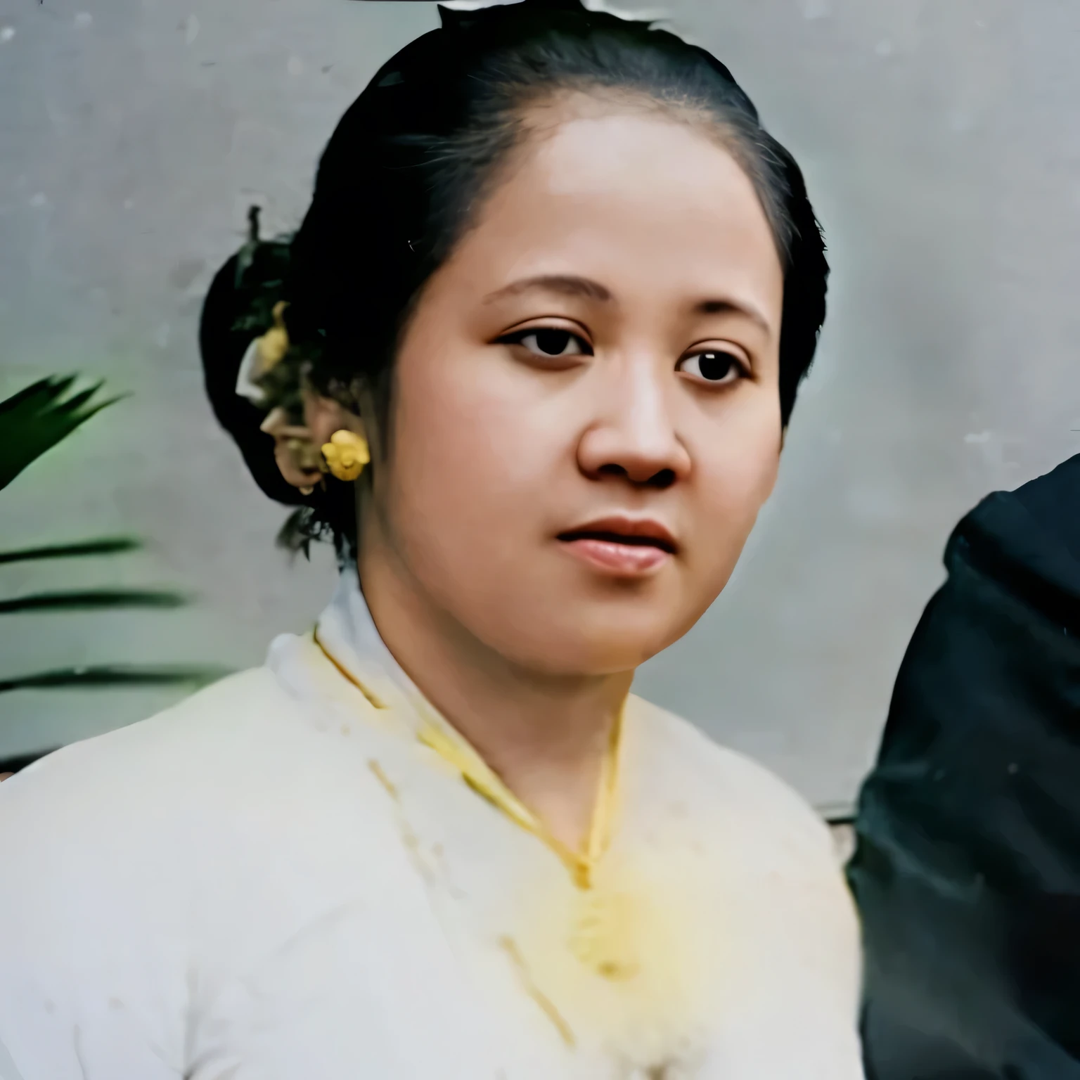 A Javanese woman wears a traditional white kebaya with a gold necklace and a round shaped pendant 