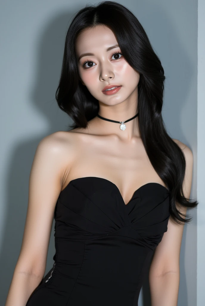 The image is a photograph of a young Asian woman with long straight black hair that cascades down past her shoulders. She has fair, smooth skin and a delicate, symmetrical face with high cheekbones, full lips, and large breasts, expressive brown eyes accentuated by subtle makeup. Her expression is shy smile, almost contemplative, as she gazes directly into the camera.
She is wearing a black, strapless dress that clings to her upper body, highlighting her slender frame. The dress has a slight sheen, suggesting it might be made of satin or a similar material. Around her neck, she wears a thin black choker with a small, sparkling silver pendant in the center, adding a touch of elegance to her look.
The background is a plain, light gray wall with no discernible features, which helps to keep the focus on the subject. The lighting is soft and even, eliminating harsh shadows and giving the image a gentle, almost ethereal quality. The overall style of the photograph is minimalist, with a focus on the subject's natural beauty and the simplicity of her attire.  