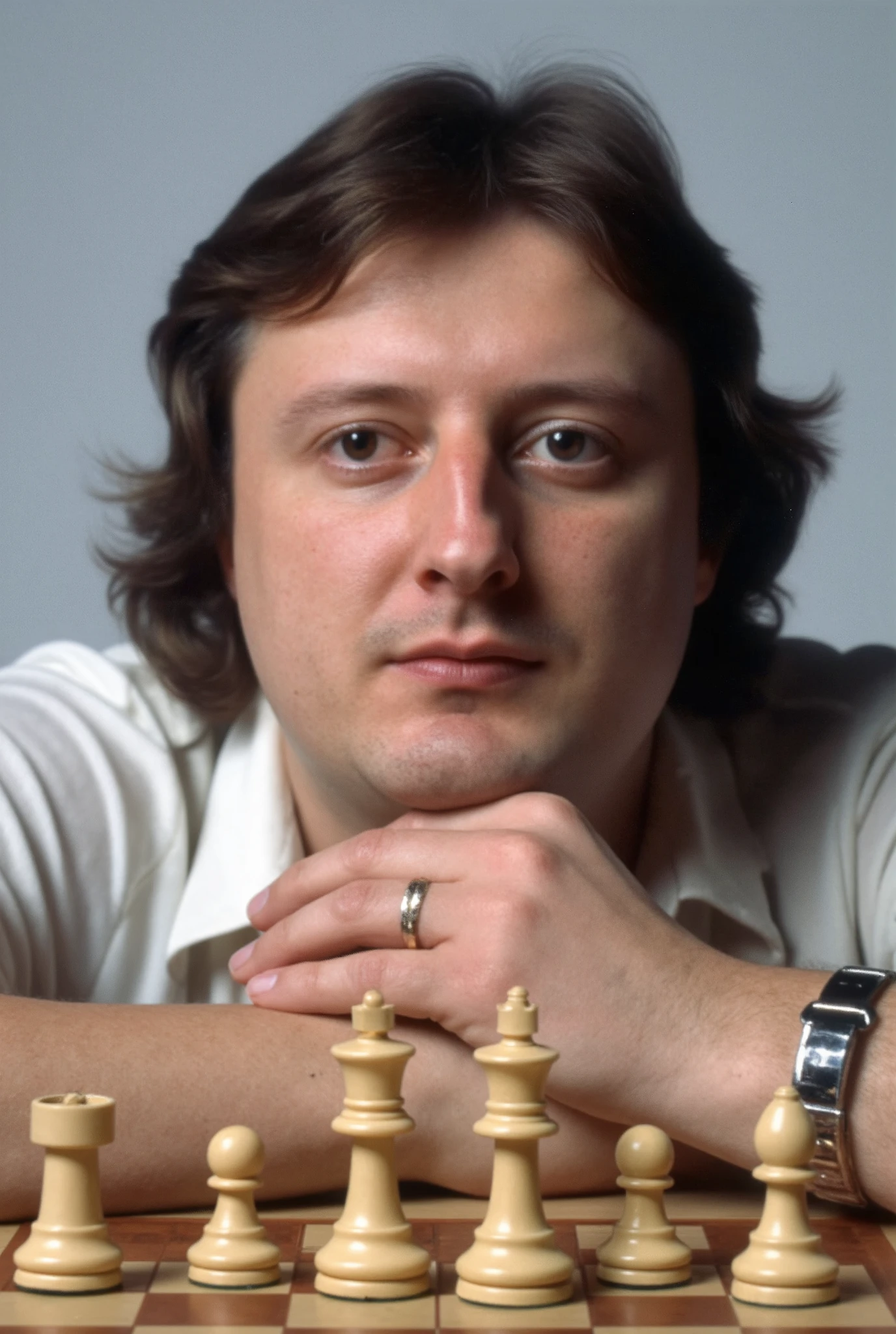 A high-resolution photograph of Eric Bristow sitting behind a chess board, chin resting on his hands, looking down contemplatively