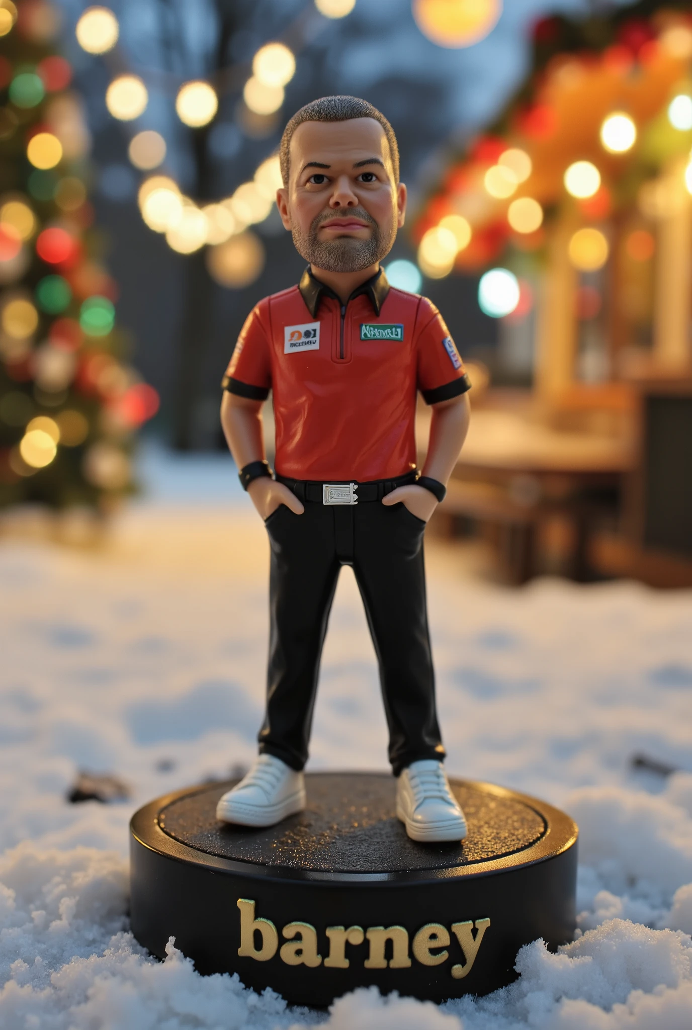 This is a high-resolution photograph of a detailed, miniature action figure of Raymond van Barneveld, standing on a round, black base. The figure, which appears to be modeled after a dart player, has a rugged, intense expression. He is wearing a darts shirt with a silver belt and black pants. The figure also wears white sneakers. The figure is positioned centrally in the image, with its hands in pockets, giving it a stance that suggests relaxation. 3d text reading "Barney" is engraved in gold in the base. The background is slightly blurred, with a bokeh effect that highlights the figure and creates a sense of depth. The background appears to be an outdoor, snowy Christmas setting, with festive lights and elements. The colors in the background are warm and vibrant, with a mix of green, whites, and red hues, suggesting it might be a park or a public space during winter. The lighting is from Christmas lights, casting soft shadows and adding a warm glow to the scene. The overall mood of the image is dynamic and focused, emphasizing the detailed and expressive miniature figure.