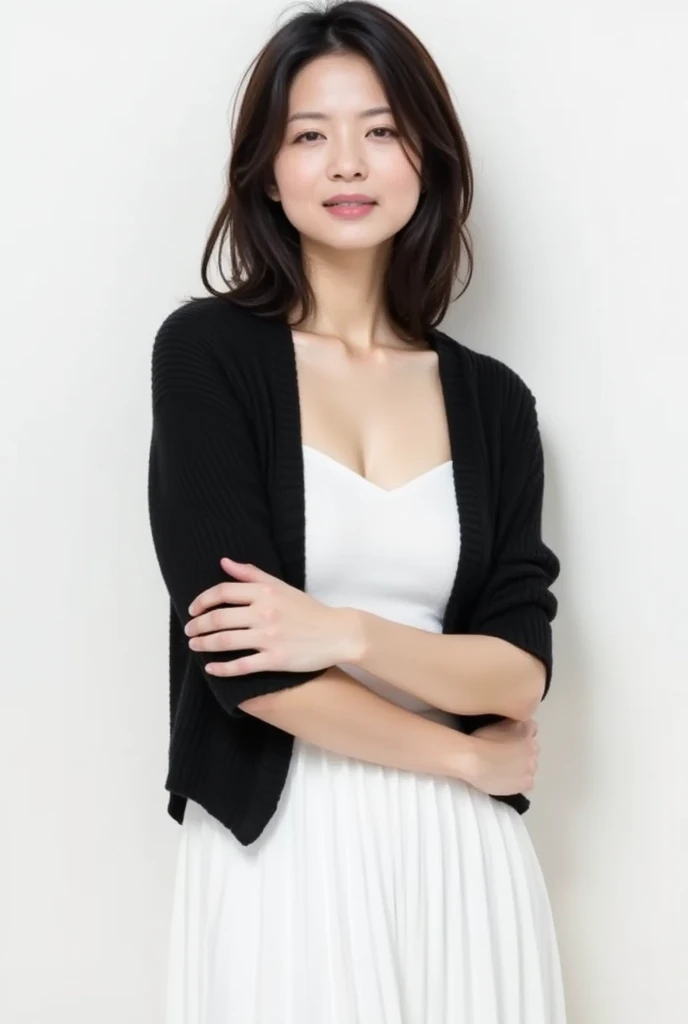 The image is a full-length portrait of a young asian woman standing with her arms crossed over her chest. She is wearing a black shawl over a white dress. The woman has shoulder-length dark hair that is styled in loose waves and falls over her shoulders. She has a neutral expression on her face and is looking directly at the camera. The background is plain white, making the woman the focal point of the image.