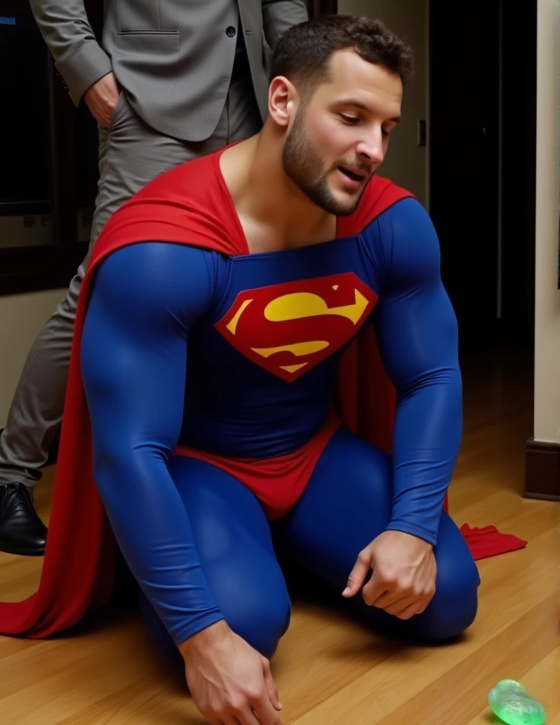 a muscular attractive h3nr4, Nick Bosw with Short stubble in a blue and red superhero costume with a prominent yellow 'S' emblem on the chest, falling to his knees on a wooden floor, orgasm face, eyes closed, mouth open, head down, small glowing green rock on the floor. Another person, only partially visible, stands nearby, wearing a gray suit and black shoes